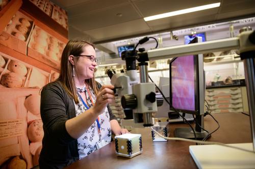 Former CCAS Corcoran student Cassie Green working at a museum desk with artifacts and stacks of pottery behind her