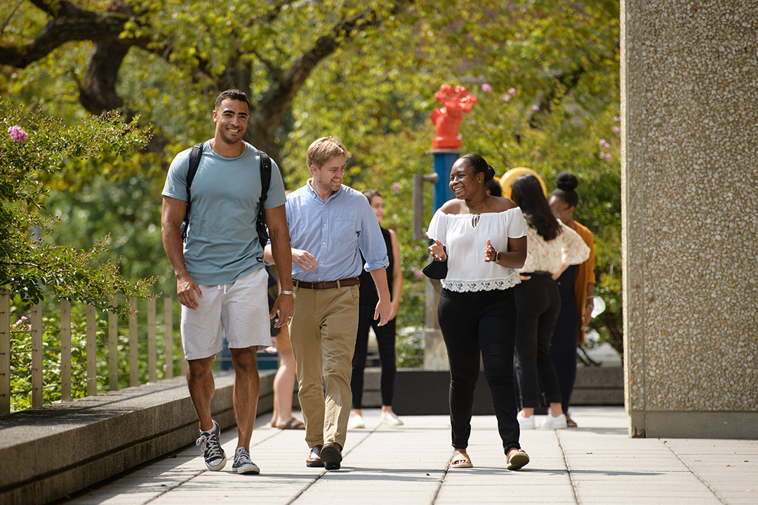 Three GW TSPPPA students walking outside a campus building with trees in the background